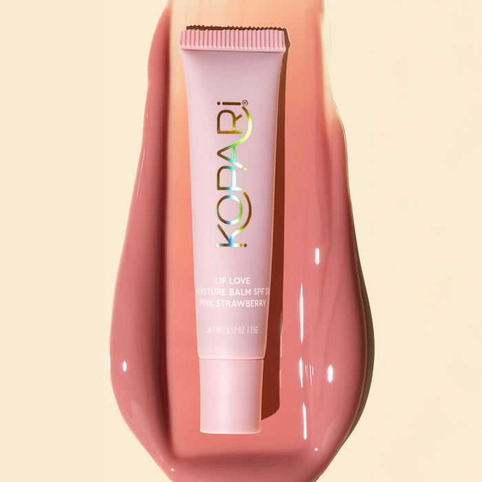 Top-down view of Kopari Lip Love moisture balm tube showing holographic logo and Pink Strawberry shade on a glossy pink product smear