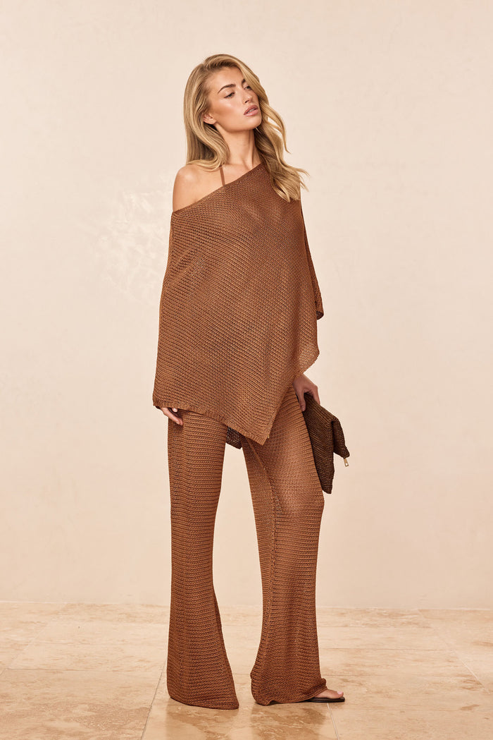 Three-quarter view of Low Rise Belize Pant in caramel treble knit showing low-rise waist and flared legs on model against a pale beige studio background