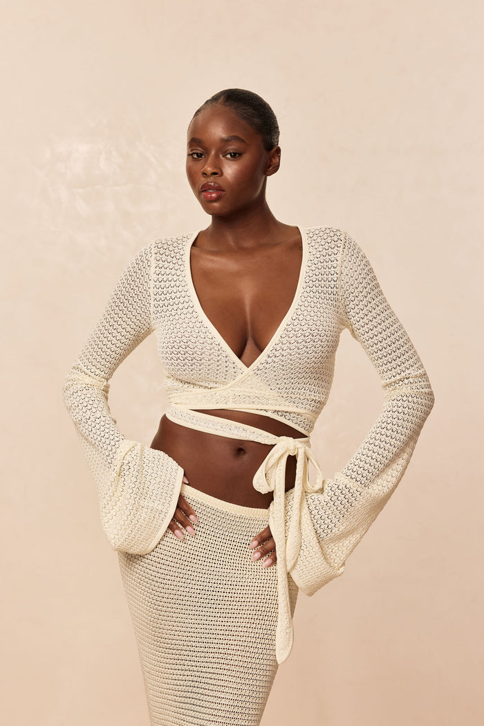 Front view of Madrid Wrap Top in ivory lace crochet showcasing V wrap, long sleeves and waist tie against beige background