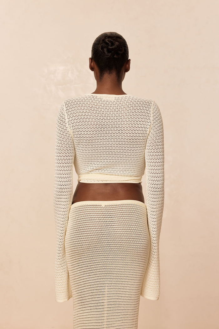 Back view of Madrid Wrap Top in ivory lace crochet, cropped wrap style with long sleeves on model against neutral background