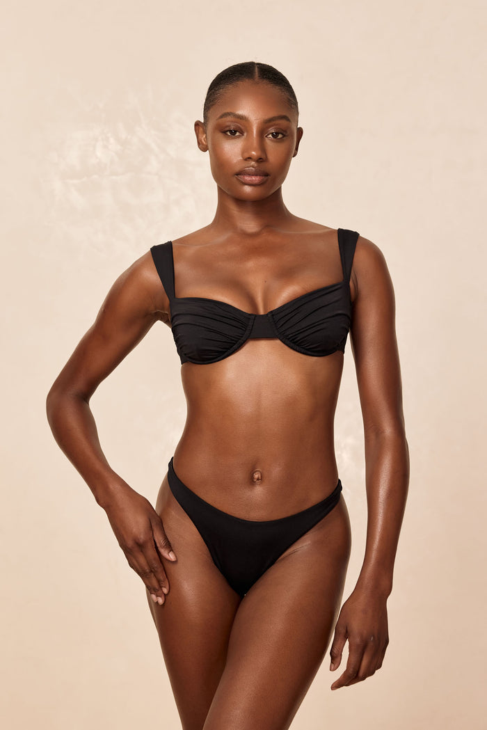 Front view of Malibu Top in black on model showcasing underwire ruched cups and wide straps against beige background