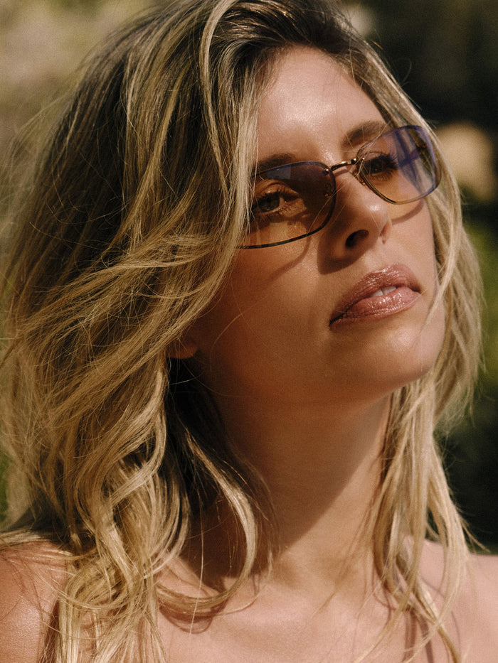 Woman wearing Malta sunglasses in bronze, gazing upward in warm outdoor light showing brown gradient lenses
