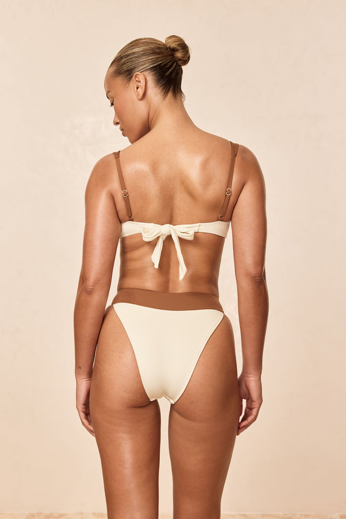 Back view of Marseille Bottom in ivory and caramel showing contrast caramel waistband and high-cut leg on beige background
