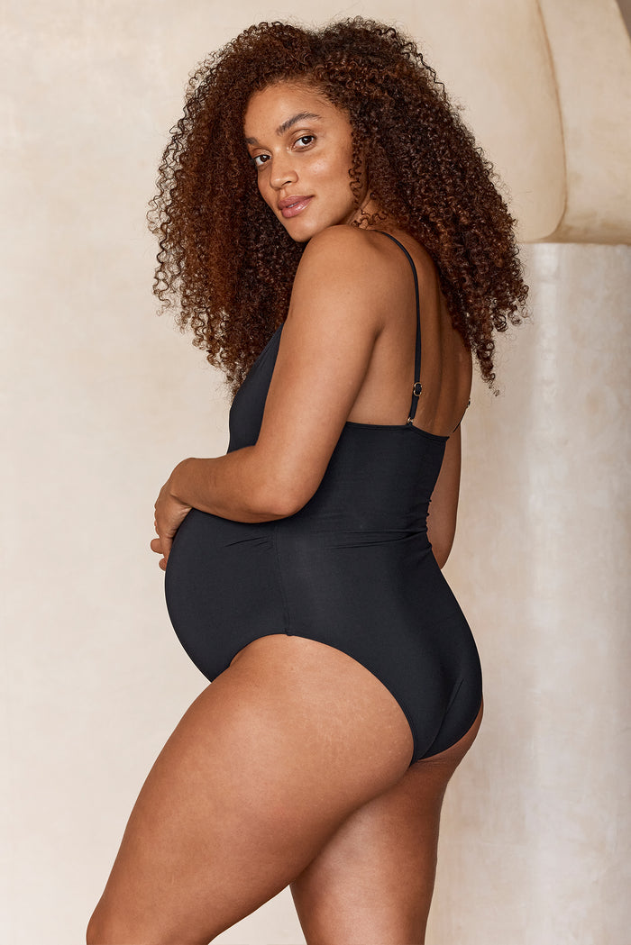 Side view of Maternity Bahamas One Piece in black showing high leg, adjustable straps, and built in bra on a pregnant model