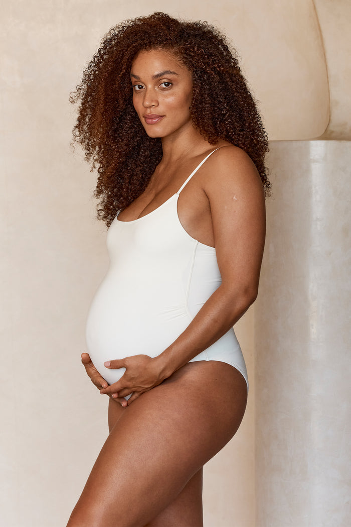 Three-quarter view of maternity Bahamas one-piece in ivory showing scoop neck, thin straps, built-in support and high leg on neutral background