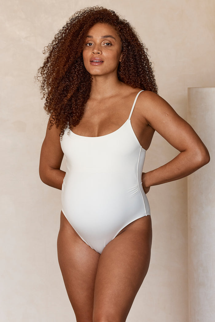 Front view of Maternity Bahamas one-piece in ivory on pregnant model showing rounded neckline, high-cut leg, maternity fit
