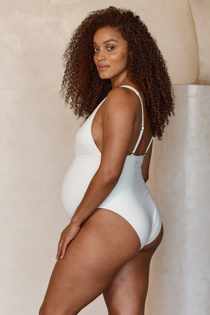 Side view of Maternity Portofino one-piece in ivory on pregnant model showing empire waist, adjustable straps, and moderate coverage