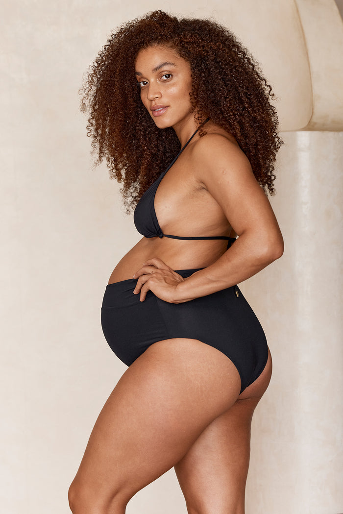 Side view of Maternity Sorrento Bottom in black with high-waist and shirred front on pregnant model, neutral background