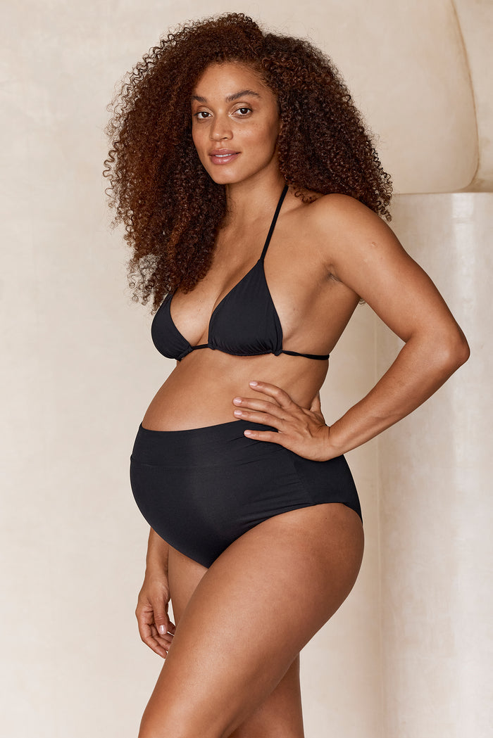 Side view of Maternity Sorrento Bottom in black on a pregnant model, high waisted maternity fit with shirred front waist, neutral background
