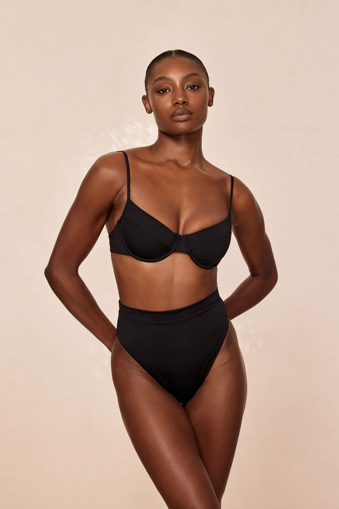 Front view of Sorrento Bottom in black showcasing high-waisted fit and moderate coverage on beige background