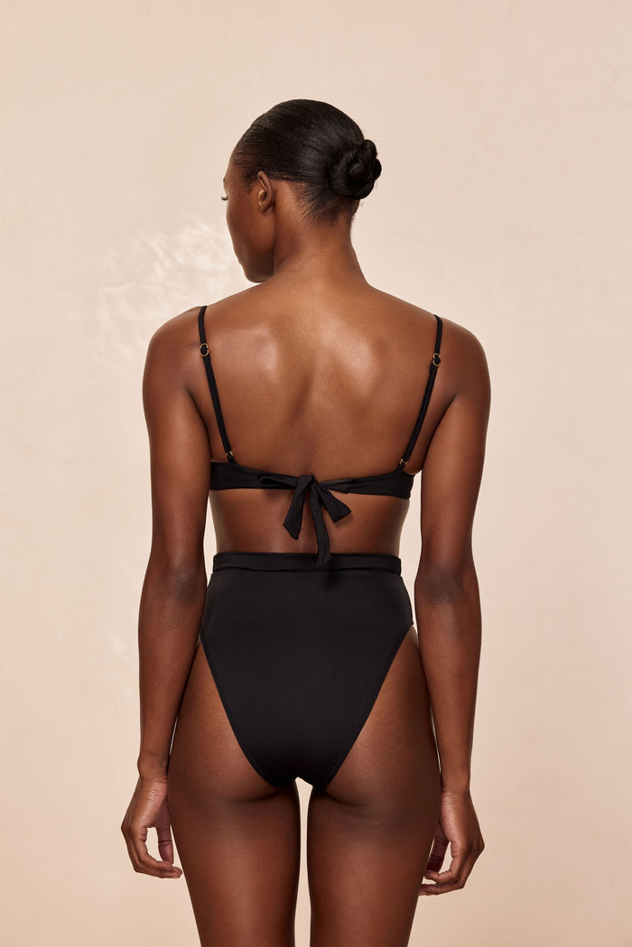 Back view of Sorrento Bottom in black showing high-waisted fit and moderate coverage on a model against a beige background