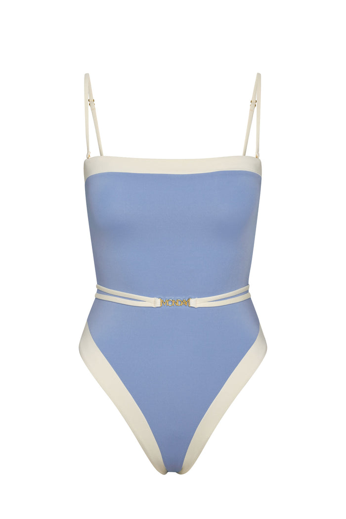 One-piece light blue swimsuit with cream trim, thin shoulder straps and a decorative belt buckle reading MONDAY.