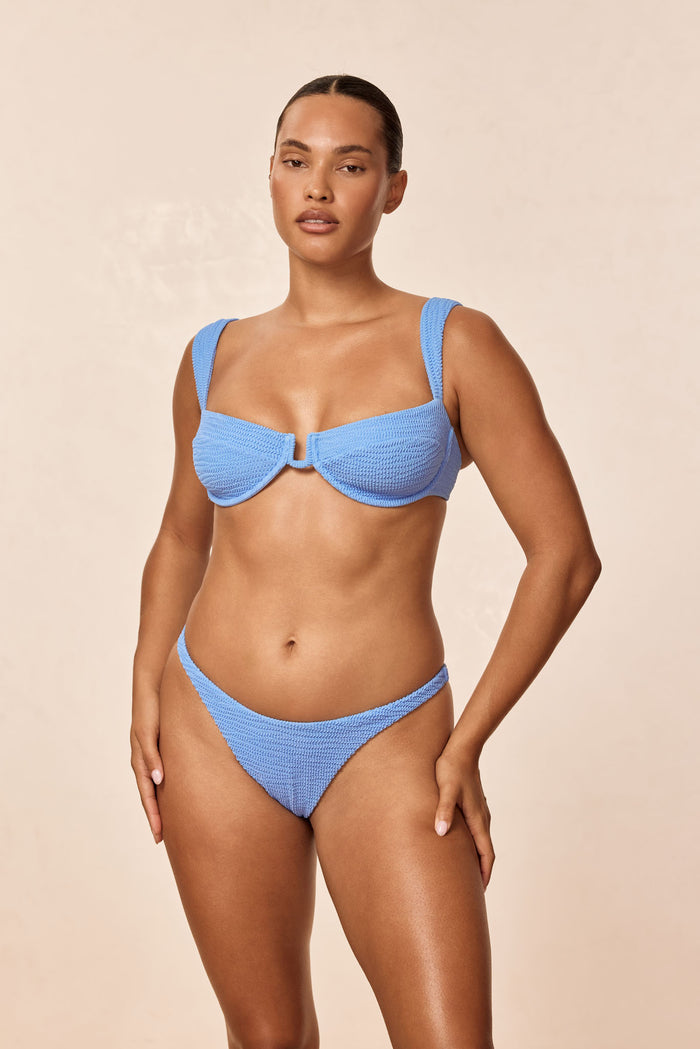 Front view of Cala Roja Top in Azure Crinkle showcasing underwire balconette shape, wide straps, and crinkle texture on model against beige background