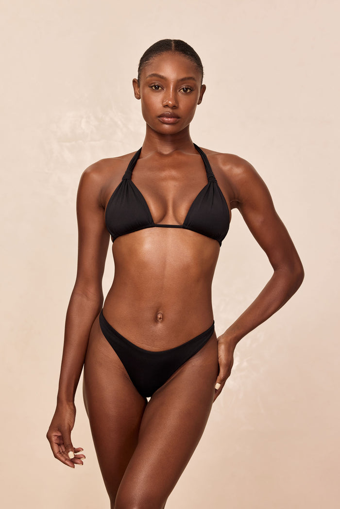 Front view of Tulum Top in black on model showcasing halter triangle cups and tied neck straps on a beige studio background