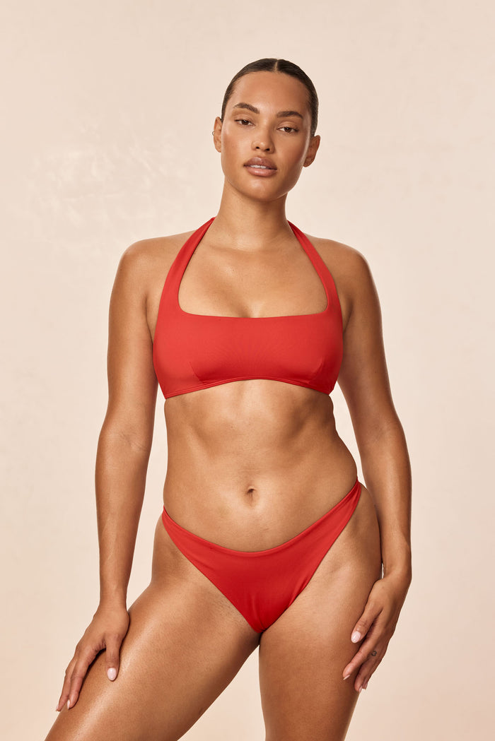 Front view of Milos Thong in Chili Pepper showcasing high-cut front and slim waistband on a model with a plain beige background
