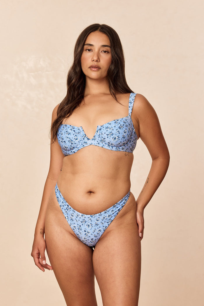 Front view of Milos Thong in Isola Floral, light blue floral thong with high-cut, cheeky fit on model against beige background