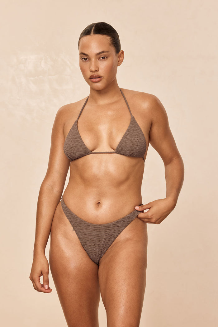 Front view of Milos Thong in Stone Crinkle showcasing seamless mid-rise thong fit on model against neutral beige background