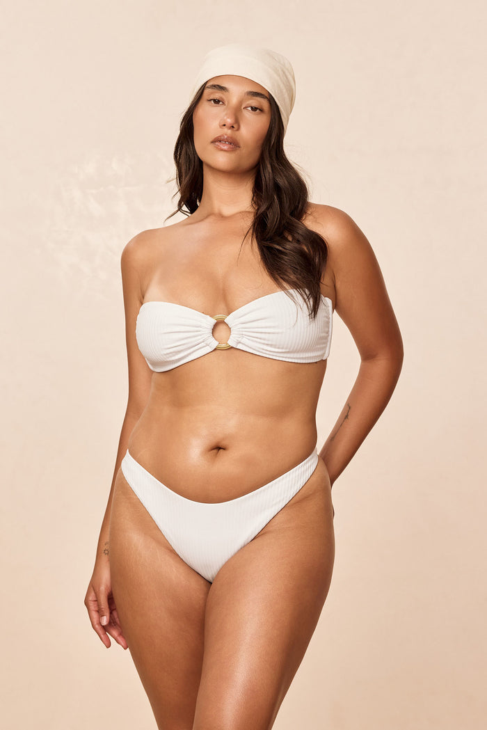 Front view of Milos Thong in White Rib on model showcasing mid-rise seamless thong cut and ribbed texture with beige background