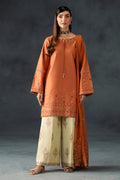 Woman wearing an orange embroidered outfit with beige pants against a dark background