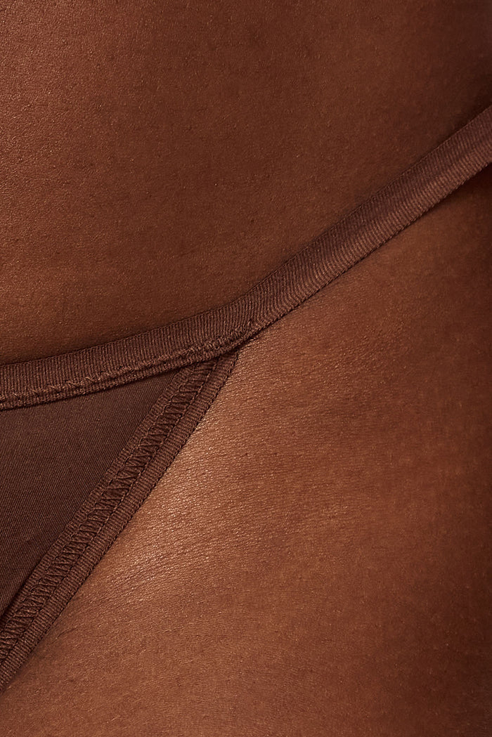 Close-up of Monday G-string in mocha showing thin side strap and minimal coverage on model's hip