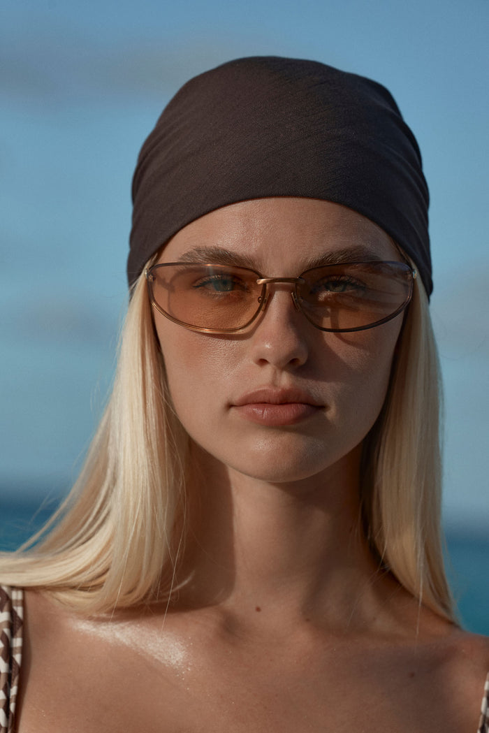Close-up front view of Monday Head Scarf Espresso showcasing a smooth square head wrap on a model with a blue ocean background