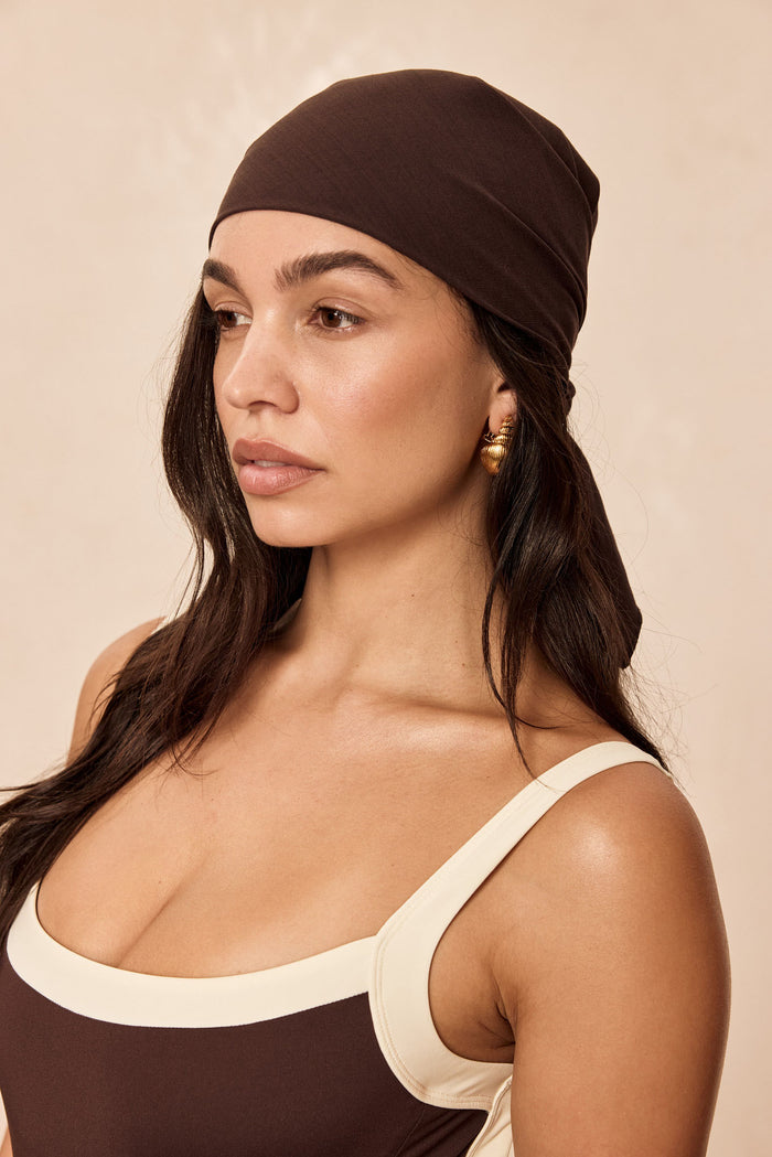 Three-quarter view of Monday Head Scarf in Espresso tied at back on model, lightweight square scarf against beige background