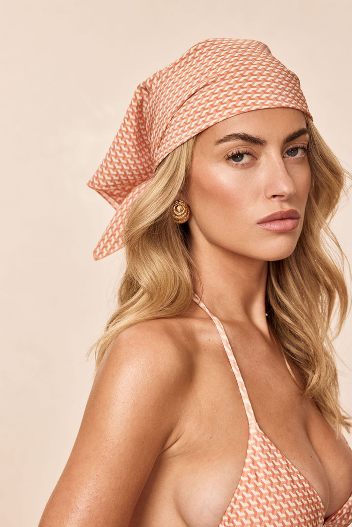 Three-quarter view of Monday Head Scarf Micro Geo silk tied at back on model, peach geometric print on beige background