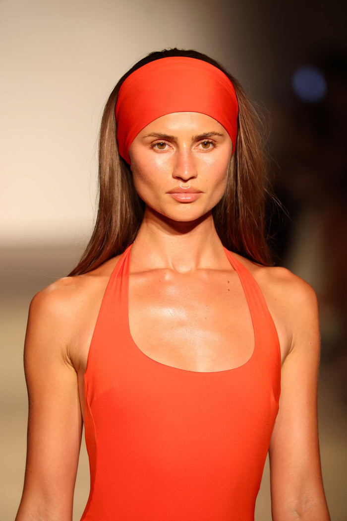 Close up front view of Monday Headband in Chili Pepper showcasing wide swim fabric band worn on model with blurred runway background