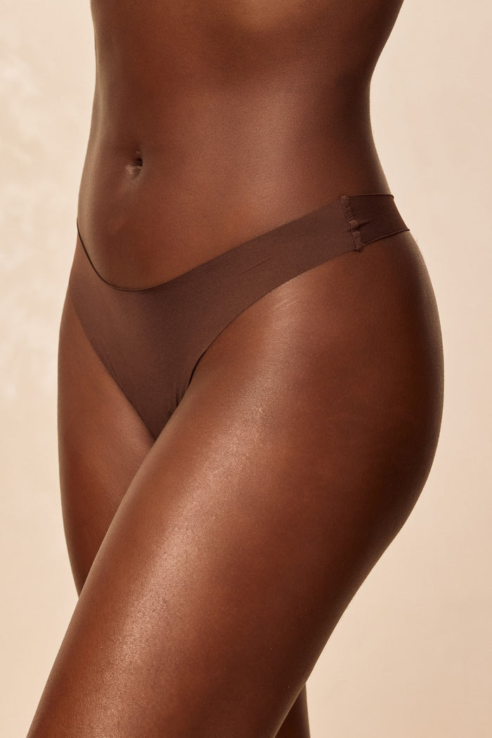 Front close-up of Invisible Thong in Mocha showing mid-rise fit and raw-edge detail on model against beige background