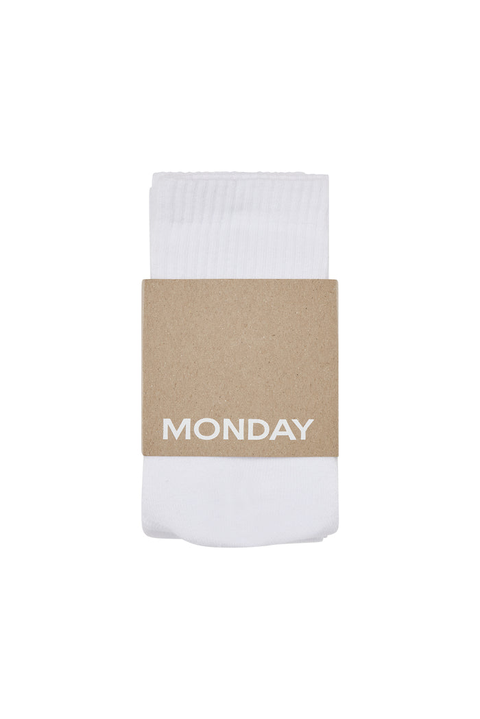 Folded white socks with a brown cardboard band labeled MONDAY