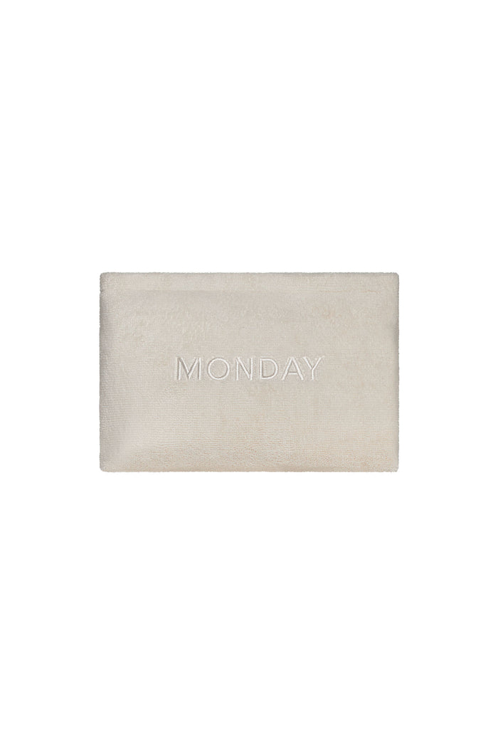 Front view of Monday Sunscreen Bag showing ivory terry exterior, tonal MONDAY embroidery, and gold zipper on white background