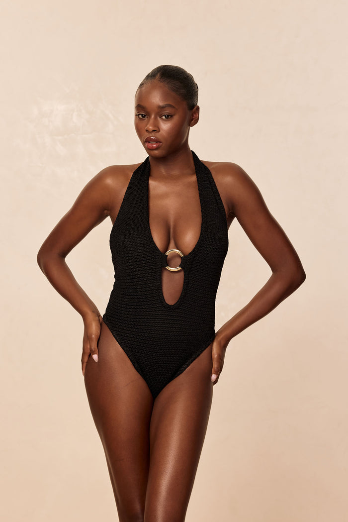 Front view of Montego Bodysuit in black treble knit with plunging halter and center gold ring on beige background