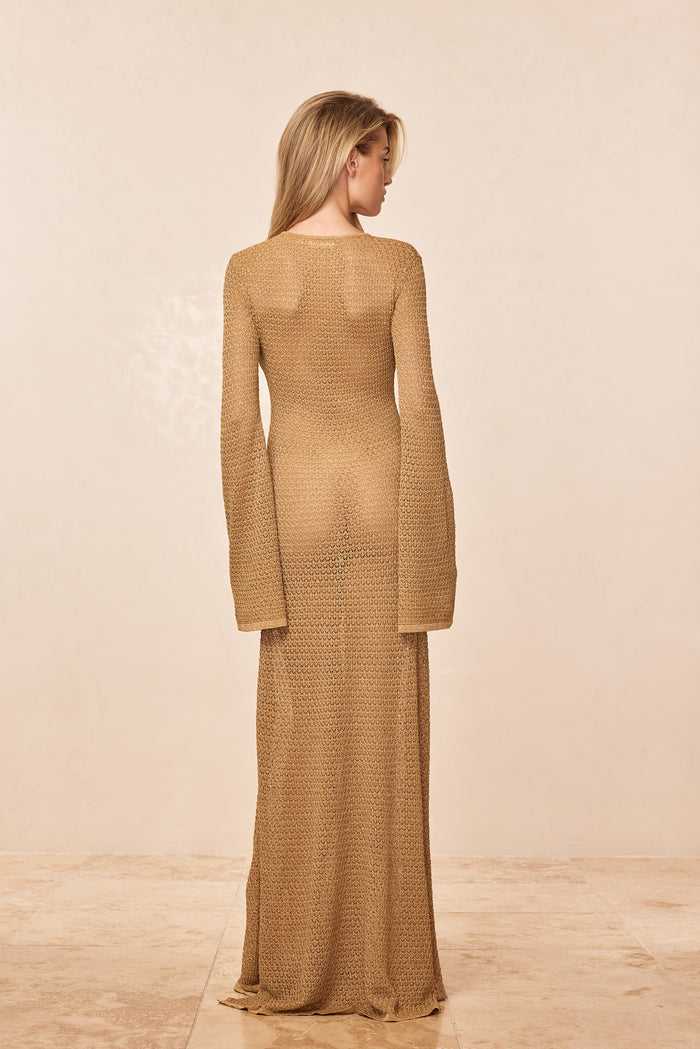 Back view of Montego dress in gold lurex crochet showing sheer knit and long bell sleeves on beige background