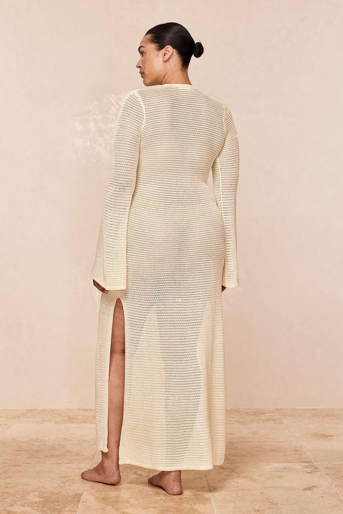 Back view of Montego Dress in ivory treble knit showing open-knit fabric, high side slit, long sleeves, studio background