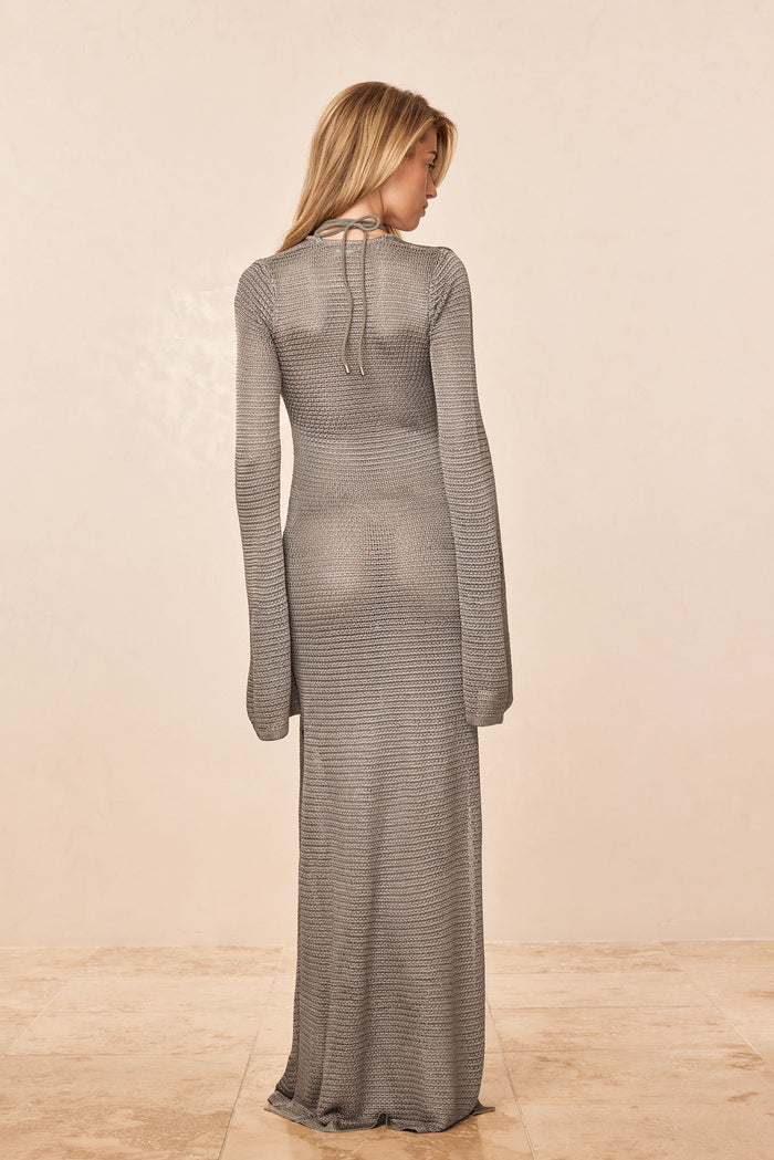 Back view of Montego Dress Steel Treble Knit showing sheer knit, long flared sleeves and halter neck tie on beige background