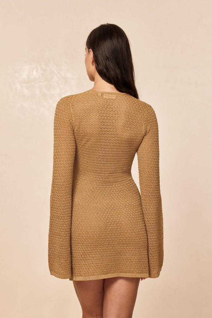 Back view of Montego Mini Dress in antique gold lace crochet showing textured knit, long sleeves, mini length on beige background