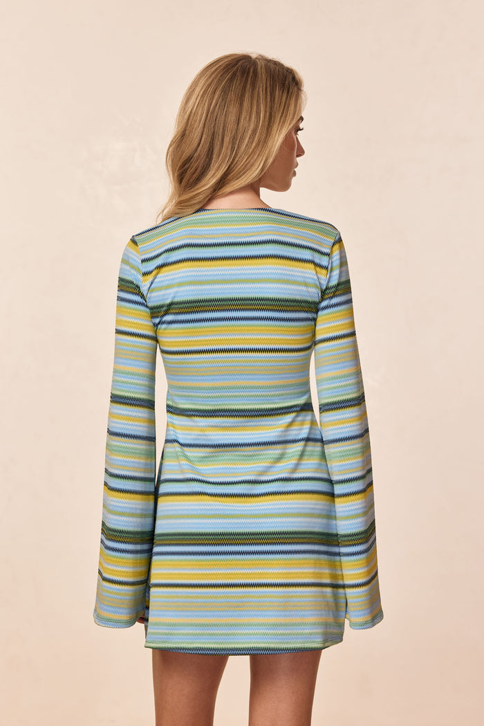 Back view of Montego mini dress in Sardinia Stripe Azure with bell sleeves and multicolor stripes on a beige background