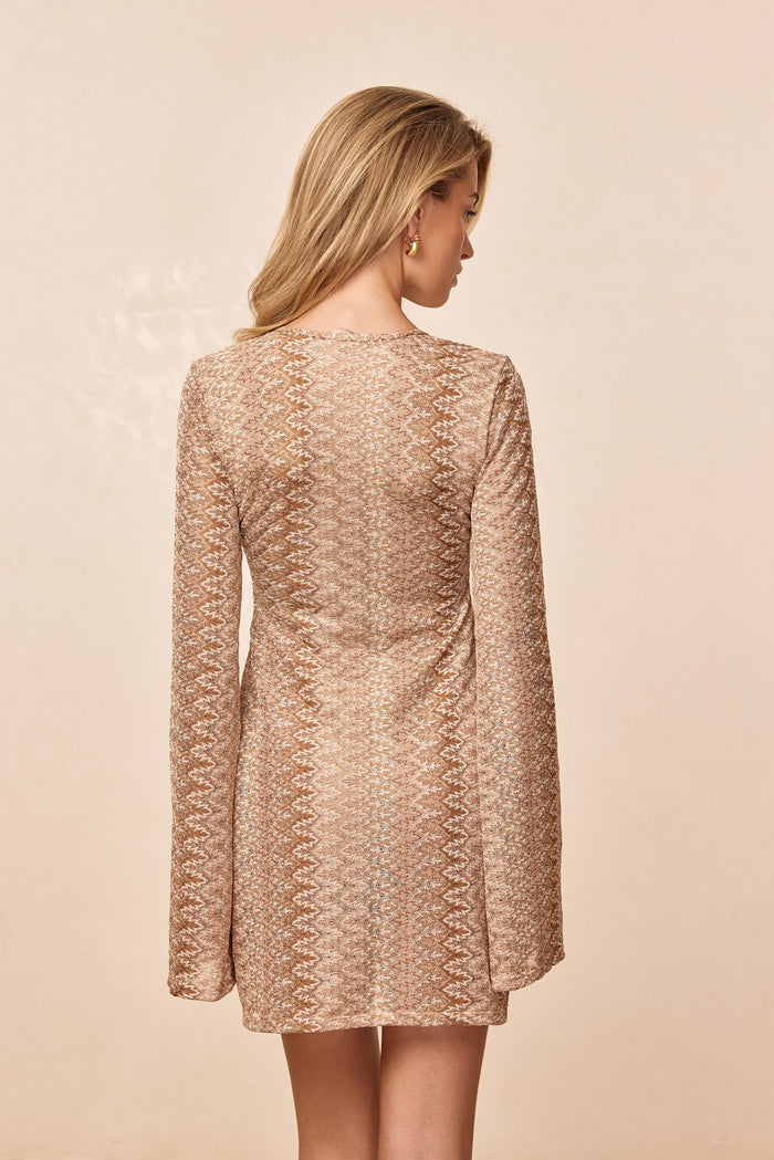 Back view of Montego Mini Tie Dress in Porto Cervo Gold showing textured metallic knit, long sleeves, and mini length on a beige background