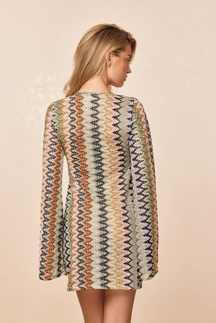 Back view of Montego Mini Tie Dress in Porto Cervo Multi with multicolor zigzag pattern and long sleeves on beige background