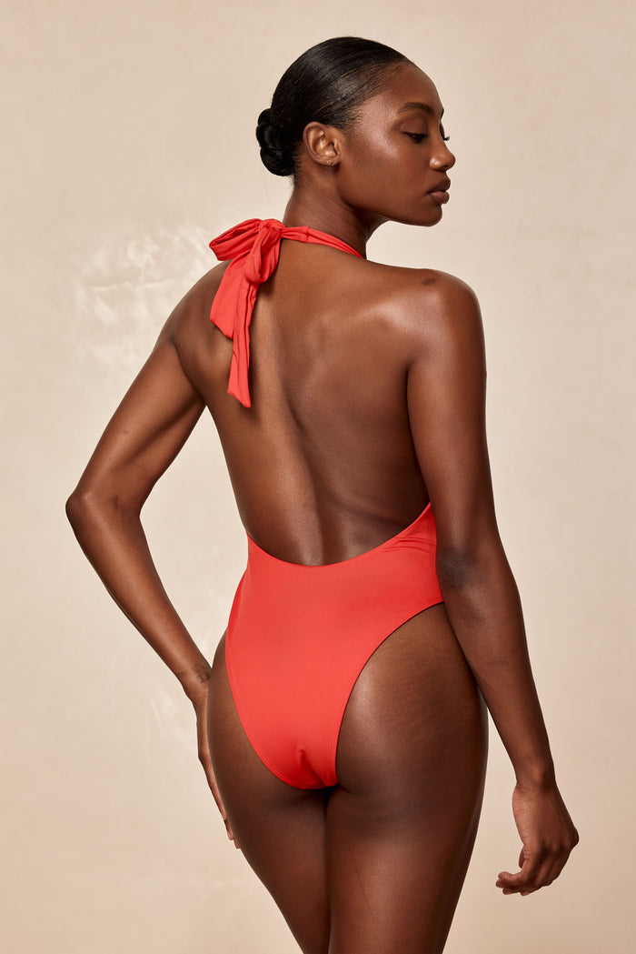 Rear view of Montego One Piece in Chili Pepper showcasing low scoop back, halter tie bow, and high-cut leg on beige background