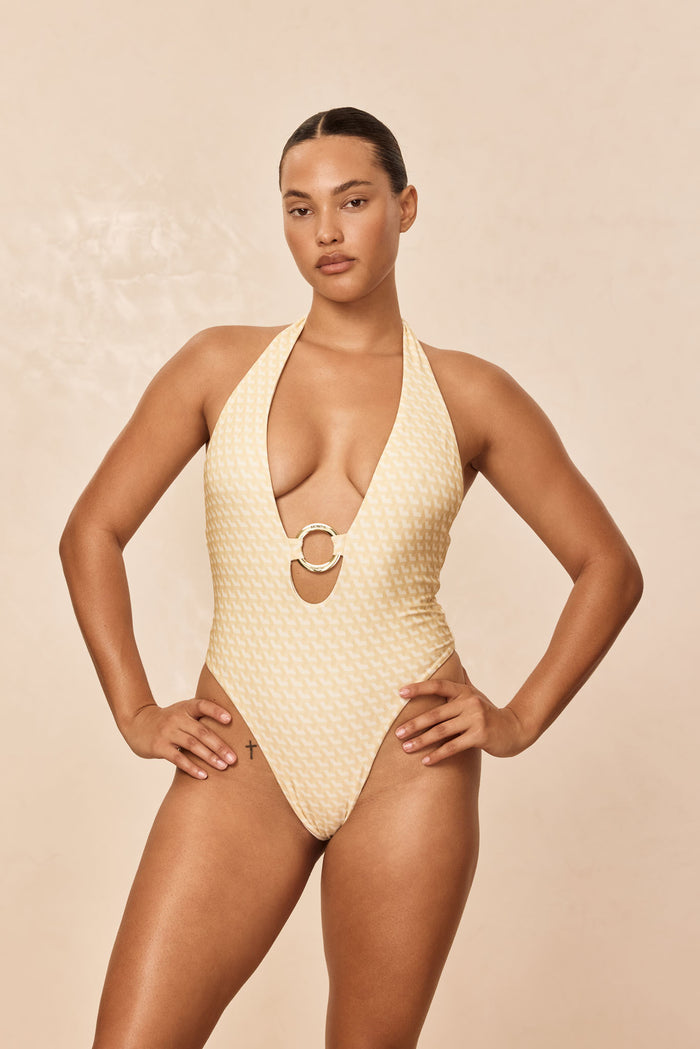 Front Montego One Piece in Ivory Geo with plunging halter neckline, gold ring center, high-cut leg on beige background