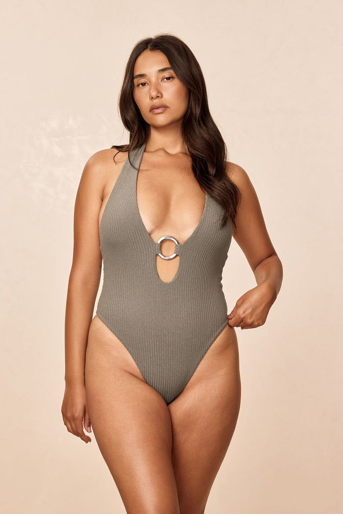Front view of Montego One Piece in Steel Lurex Rib on model, showing halter plunge, center front branded metal ring and high-leg cheeky fit with neutral beige background