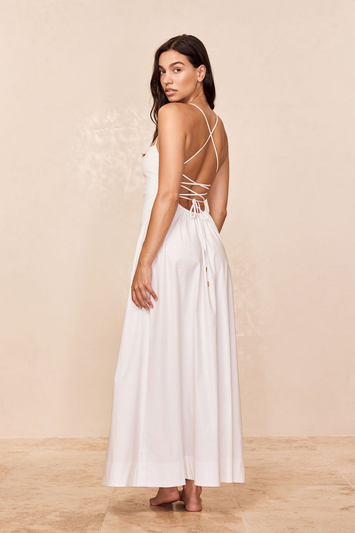 Woman looking over her shoulder wearing a floor-length white dress with crisscross back straps and waist tie
