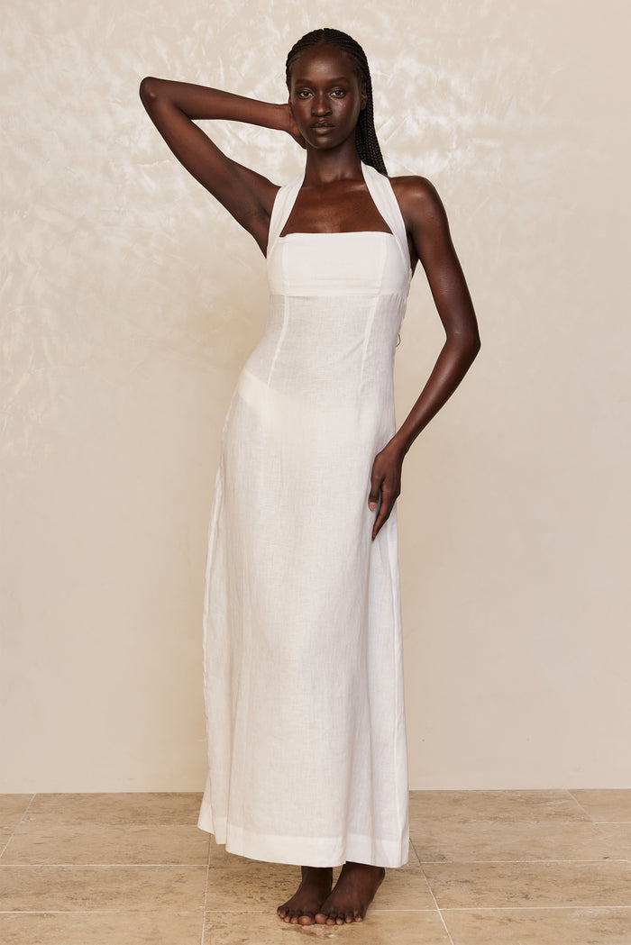 Front view of Montserrat dress in white linen showcasing halter neckline and floor-length skirt against a neutral textured backdrop