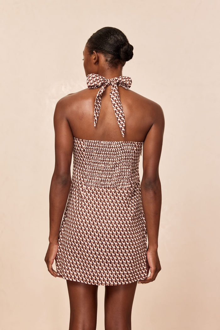 Back view of Montserrat Mini Dress in Husk Geo print showing smocked back and halter tie bow on beige studio background