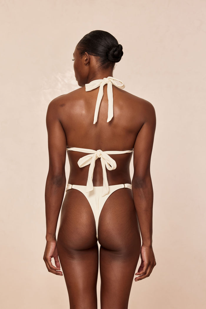 Rear view of Morocco Bottom in Ivory showcasing high-cut thong back and metal ring hip details on a neutral beige background