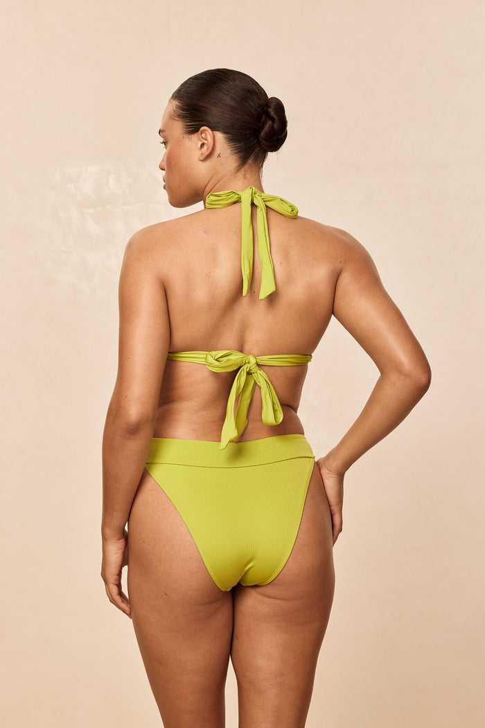 Rear view of Marseille bottom in Apple green on model showing high‑leg cut, shirred V-front waist and cheeky coverage on a beige background