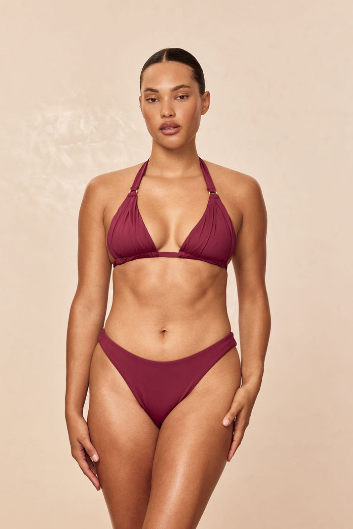 Front view of Morocco Top in fig on model showing pleated cups, gold rings and adjustable halter ties, beige background