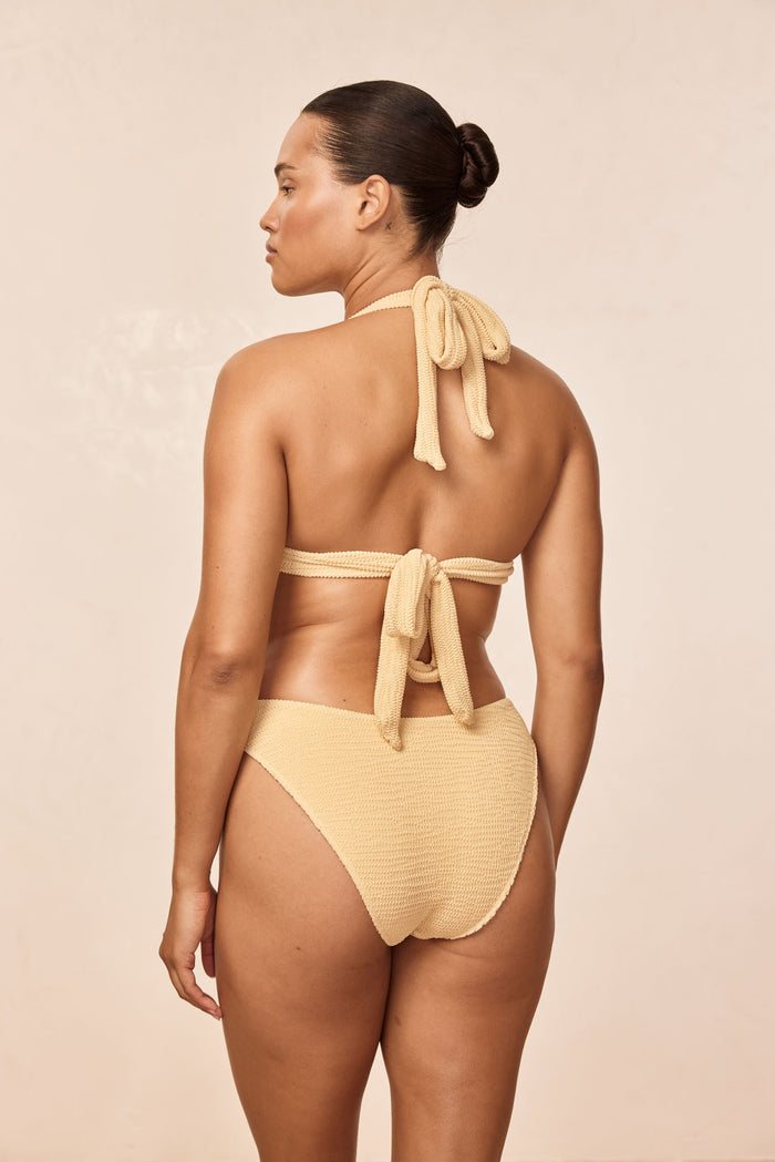 Back view of Morocco Top Raffia Crinkle on model showing tied neck and back ties, pleated cup detail on beige background