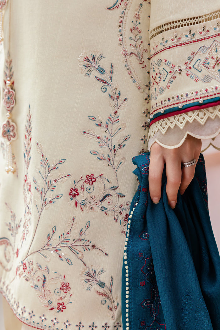 Close-up of a person wearing a cream-colored embroidered dress with floral patterns, holding a blue fabric.